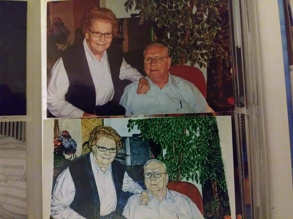 A reference photograph of an older couple displayed above Jeremy Wylie's finished portrait